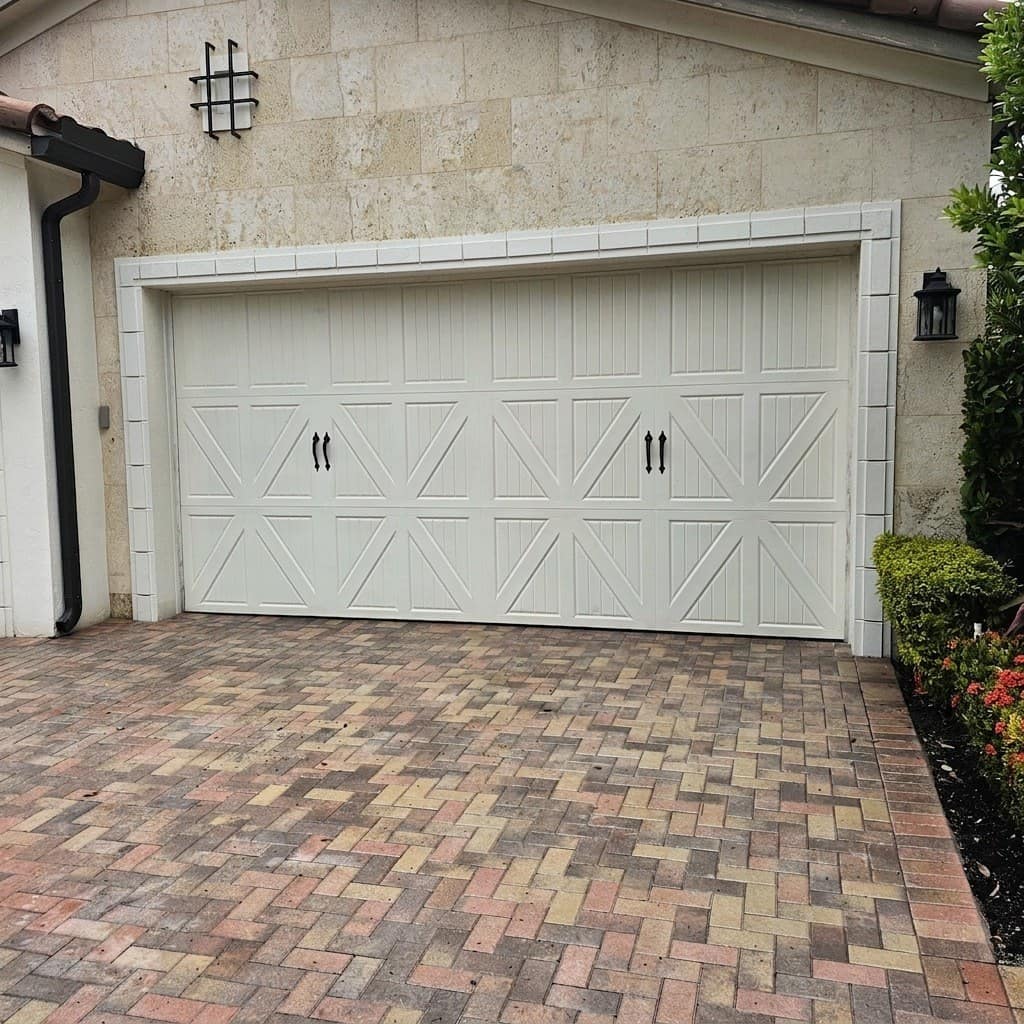 White carriage-style double garage door installed on a coral-stone house with a paver driveway